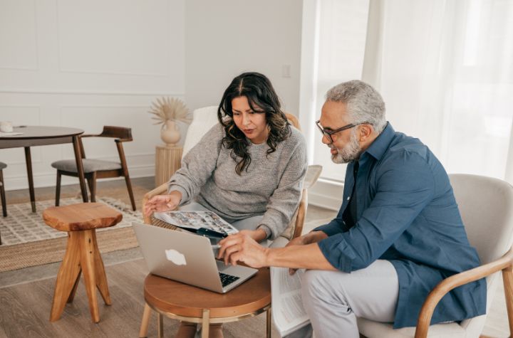 Couple sitting together and reviewing financial information on a laptop in a bright living room.