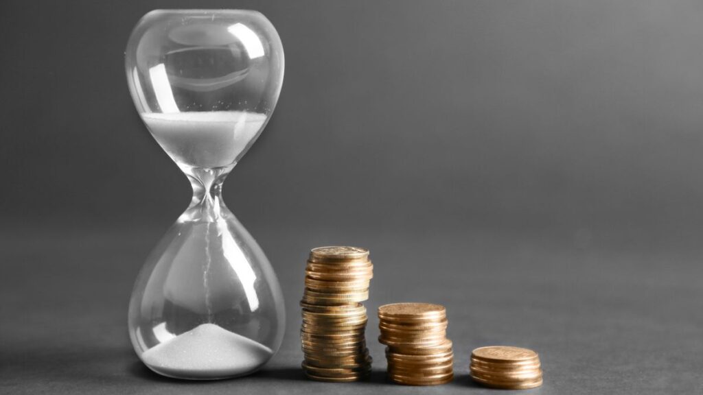 An hourglass next to rising stacks of coins representing time and compound interest growth