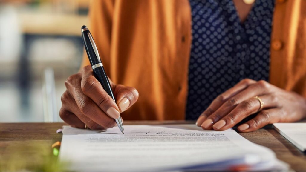 Close-up of hands signing estate planning documents on a wooden table
