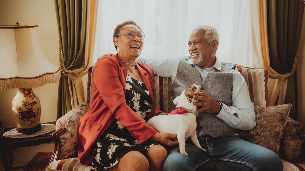 Smiling older couple on a couch with their dog, reflecting life milestones