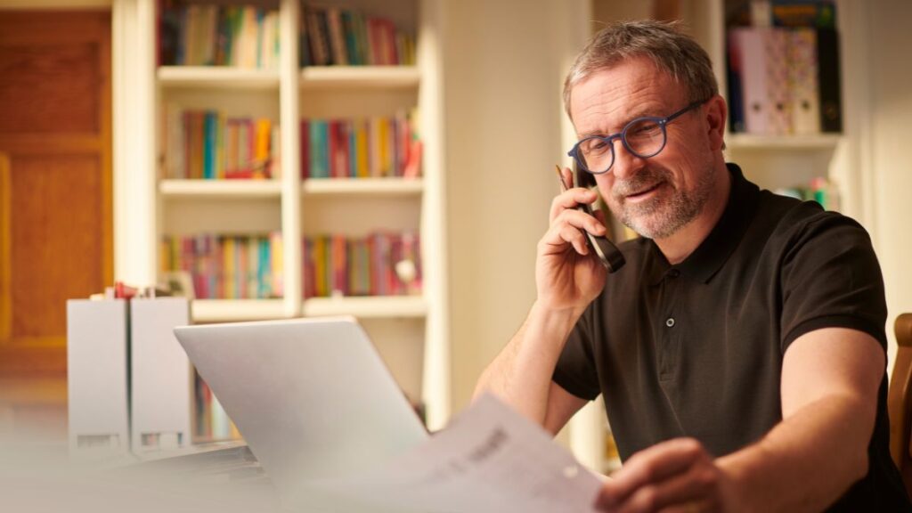 Middle-aged man reviewing business paperwork while on the phone in a home office